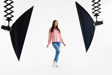Joyful lady model in casual attire mid-twirl in well-equipped photo studio with white backdrop