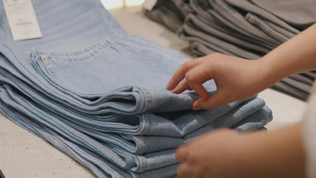 Female hands choosing clothes jeans in a clothing store shop.