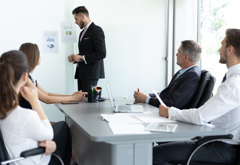 Business man presenter team leader wearing suit giving presentation training on whiteboard in office. Male company executive manager presenting corporate strategy at group conference meeting