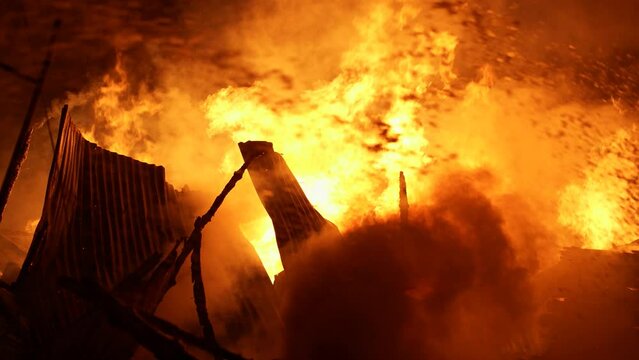 Firefighters bravely spray water on a massive fire in a rural market, using high-pressure hoses to extinguish the intense flames. Safety and disaster response are critical as they battle the blaze