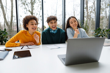 Joyful diverse students laughing at content on laptop