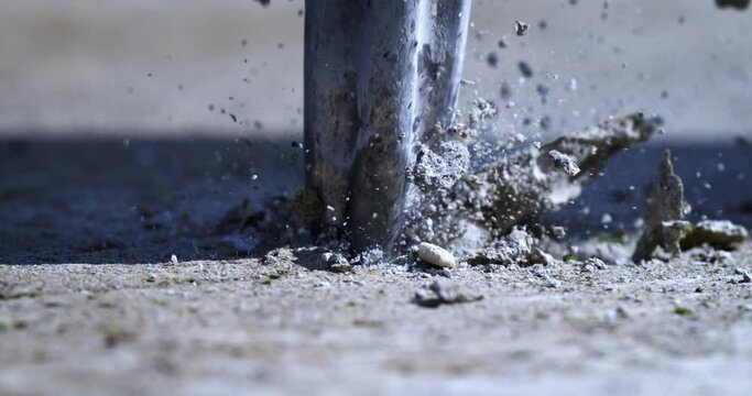 Super slow motion close up of laborer worker drilling concrete asphalt with jackhammer bit while working on road maintenance repair with flying concrete stones pieces and sand dust at 1000 fps.