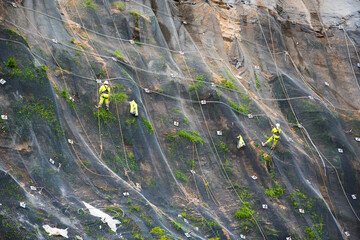 Workers strengthen the slope of the mountain with a metal mesh preventing rockfall on the road....