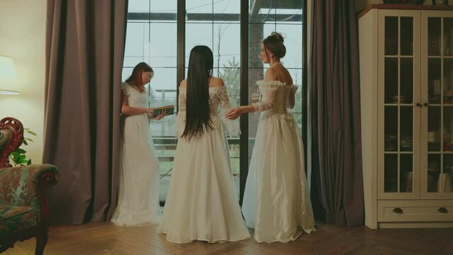 Friends group of happy women at social party lady talking gossip near window. girl reads book. Classic interior royal luxury room castle medieval event historical ball party. Long evening white dress.