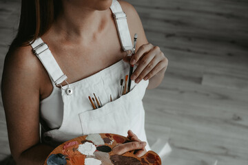 portrait of a  woman artist in a white sundress with a palette for paints and brushes for painting