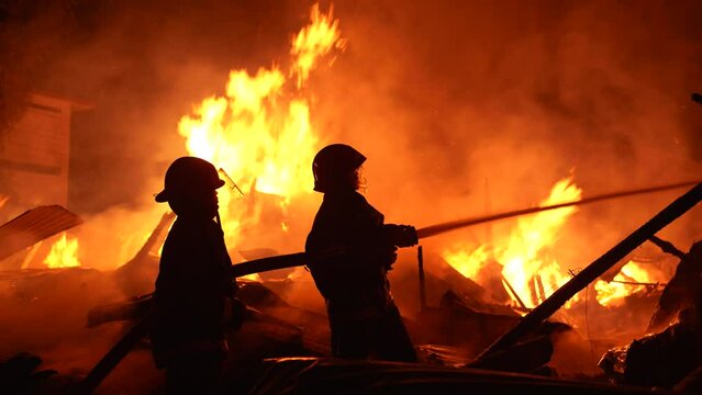Firefighters bravely spray water on a massive fire in a rural market, using high-pressure hoses to extinguish the intense flames. Safety and disaster response are critical as they battle the blaze