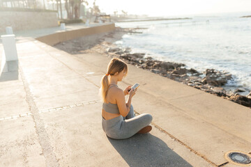 woman sitting on the pier looking into the phone reading something 
