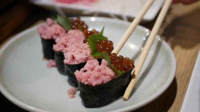close up view while using chopstick to pickup ikura with tuna sushi from the plate in japanese food style