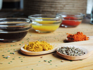 On a wooden cutting board, several wooden spoons with colorful spices such as turmeric, paprika, paprika, and cumin with various sauces in a glass jar at the bottom.