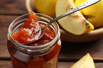 Taking tasty homemade quince jam from jar at table, closeup