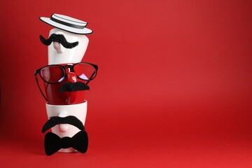 Men's faces made of cups, fake mustaches, glasses, hat and bow tie on red background. Space for text