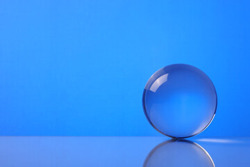 Transparent glass ball on mirror surface against blue background. Space for text
