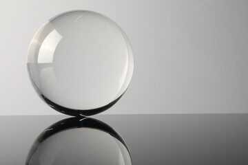 Transparent glass ball on mirror surface against light background. Space for text
