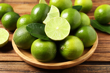 Fresh ripe limes and green leaves on wooden table, closeup