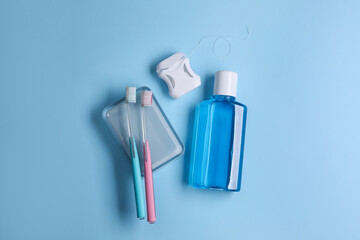 Fresh mouthwash in bottle, toothbrushes and dental floss on light blue background, flat lay