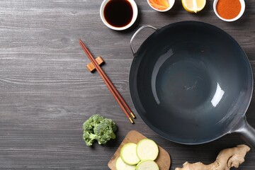 Empty iron wok, chopsticks and ingredients on grey wooden table, flat lay. Space for text