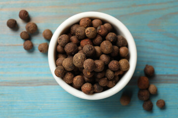 Aromatic allspice pepper grains in bowl on light blue wooden table, top view