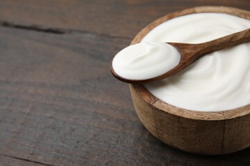 Delicious natural yogurt in bowl and spoon on wooden table, closeup. Space for text