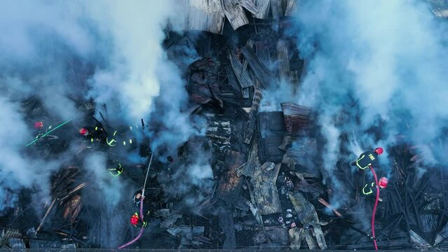 Firefighters bravely spray water on a massive fire in a rural market, using high-pressure hoses to extinguish the intense flames. Safety and disaster response are critical as they battle the blaze