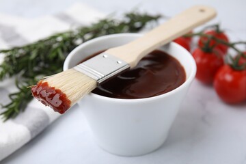 Marinade in bowl and basting brush on white table, closeup