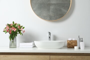 Fototapeta na wymiar Vase with beautiful Alstroemeria flowers and toiletries near sink in bathroom