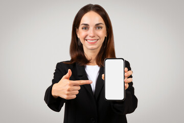 Friendly businesswoman presenting a smartphone with a blank screen and pointing at it