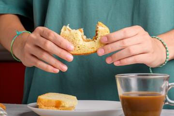 Female hands holding a bitten peanut butter sandwich with honey of wheat bread, have a breakfast. Woman faceless in petrol green colored t-shirt with bitten sandwich. Typical morning breakfast