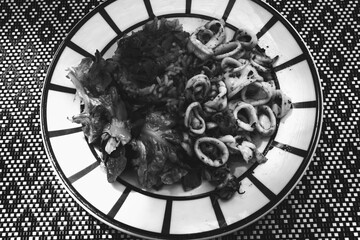 Gourmet dish at traditional French Basque country restaurant. Squids, rice with ratatouille, fresh green salad aesthetically served. Black white retro vintage graphic photo.