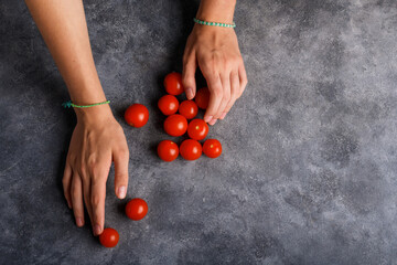 Woman hands with ripe tomatoes cherry on the gray table background, closeup. Handful of fresh red...