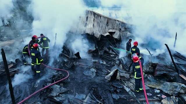 Firefighters bravely spray water on a massive fire in a rural market, using high-pressure hoses to extinguish the intense flames. Safety and disaster response are critical as they battle the blaze