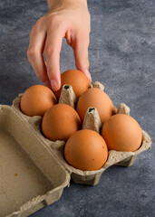 A woman's hand takes an egg from the egg box that is on the gray kitchen table, close up, food lifestyle, cooking blog
