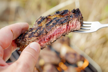 A detailed view of a hand holding a perfectly grilled steak on a fork, showcasing the charred exterior and juicy interior with precise clarity, set