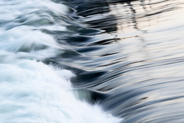 Rapid water flow over barrier with silky surface, river overflow over dam close up with splash and...