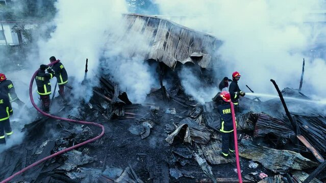 Firefighters bravely spray water on a massive fire in a rural market, using high-pressure hoses to extinguish the intense flames. Safety and disaster response are critical as they battle the blaze