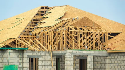 Fotobehang Street view of new wooden roof in progress, with panels of particle board on framework of trusses, atop the concrete shell of a single-family suburban house under construction in southwest Florida © Kenneth