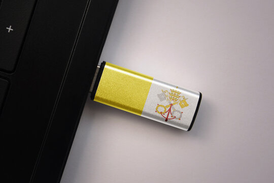 usb flash drive in notebook computer with the national flag of vatican city on gray background.