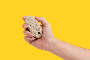 Pumice stone for cleaning feet and heels, in hand on yellow background.