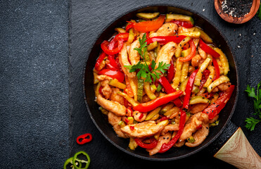 Stir fry turkey breast with red paprika and zucchini with sesame seeds, garlic, ginger and soy sauce in frying pan. Black table background, top view