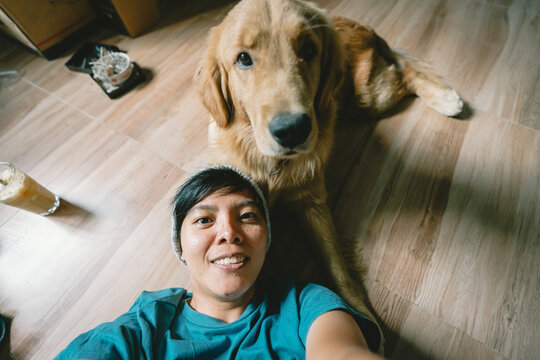 person,  real Asian man takes a selfie with a 7-month-old golden retriever. The dog is playing together Looking funny at the camera at home. Top view