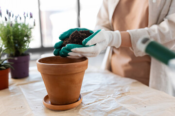 people, gardening and housework concept - close up of woman in gloves pouring soil to flower pot at home - 755866842