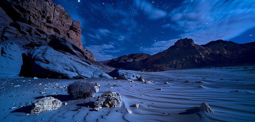 A desert scene at night, illuminated by the soft light of the moon, showcasing the contrast of cool blue sands against dark brown rocks - Powered by Adobe