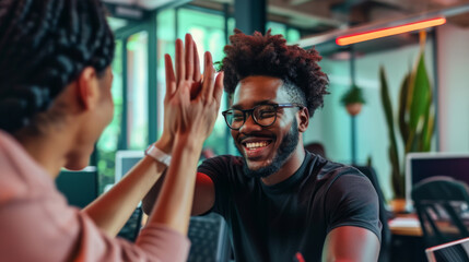 Young man with an afro hairstyle and glasses is smiling and giving a high-five in a casual office or coworking space environment.