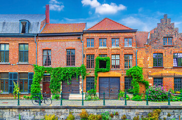 Old buildings with windows and plants on brick walls on cobblestone embankment promenade in Ghent...