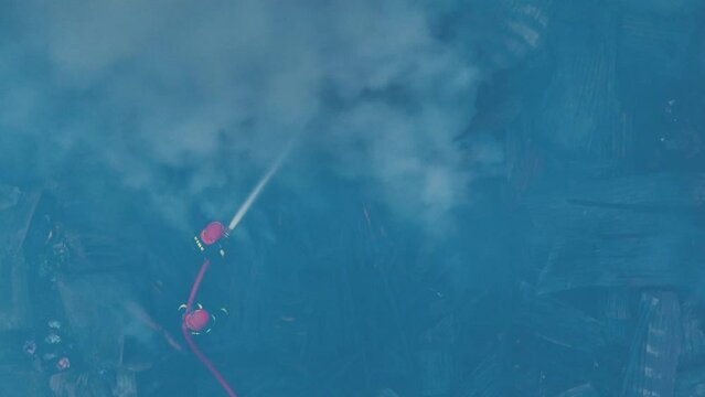 Firefighters bravely spray water on a massive fire in a rural market, using high-pressure hoses to extinguish the intense flames. Safety and disaster response are critical as they battle the blaze