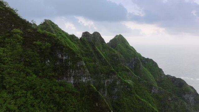 Green jungle mountains with Jurassic period scene. Dramatic nature landscape on gloomy rainy day. Kualoa park with Jurassic volcano nature.Hawaiian island coast line with steep tropical mountain ridge