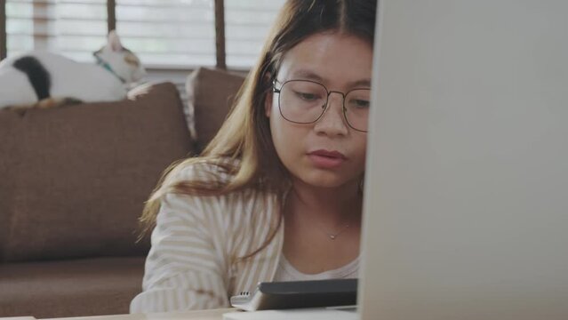 Close-up of Asian woman working from home using laptop. Checking many documents on the table