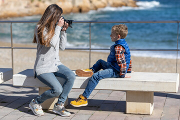 Mother taking a photo of her son, with a reflex camera, by the sea