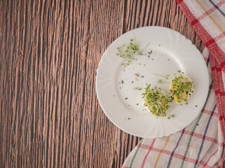 Microgrown arugula sprouts on a cut chicken egg snack on a white plate, a wooden table, a kitchen napkin with red stripes. The concept of proper nutrition and healthy snacks