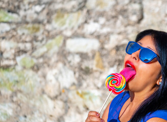 Sexy Latin woman wearing sunglasses and bright red sensual lips passionately licking a colorful...