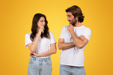 A contemplative young couple in white t-shirts and jeans, looking at each other with thoughtful expressions